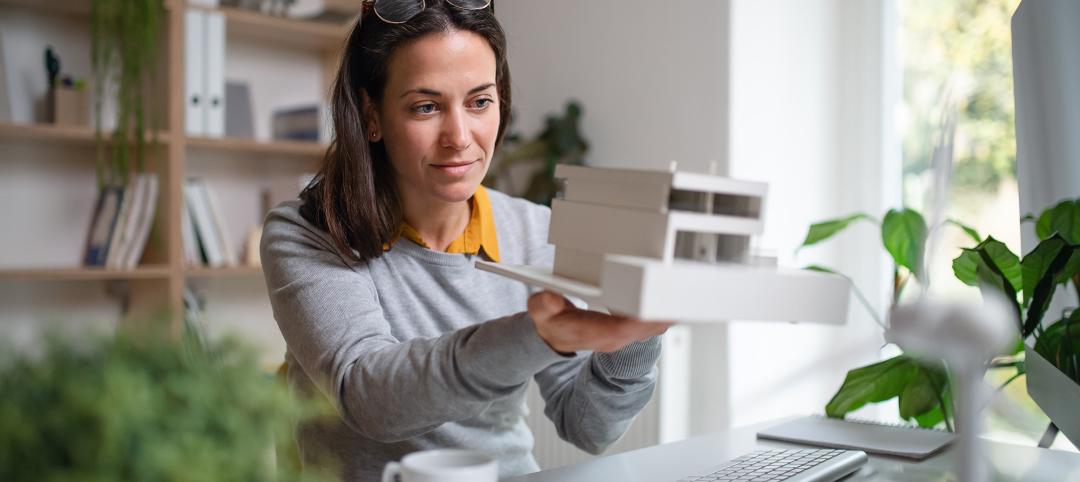 Architect with model of a house sitting at the desk indoors in office