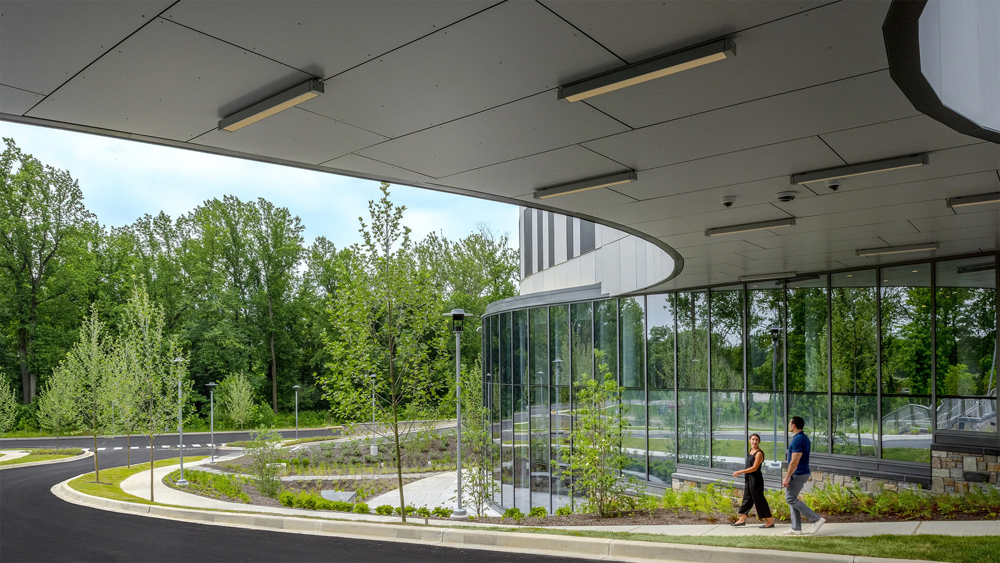 People walking outside of glass building surrounded by foliage