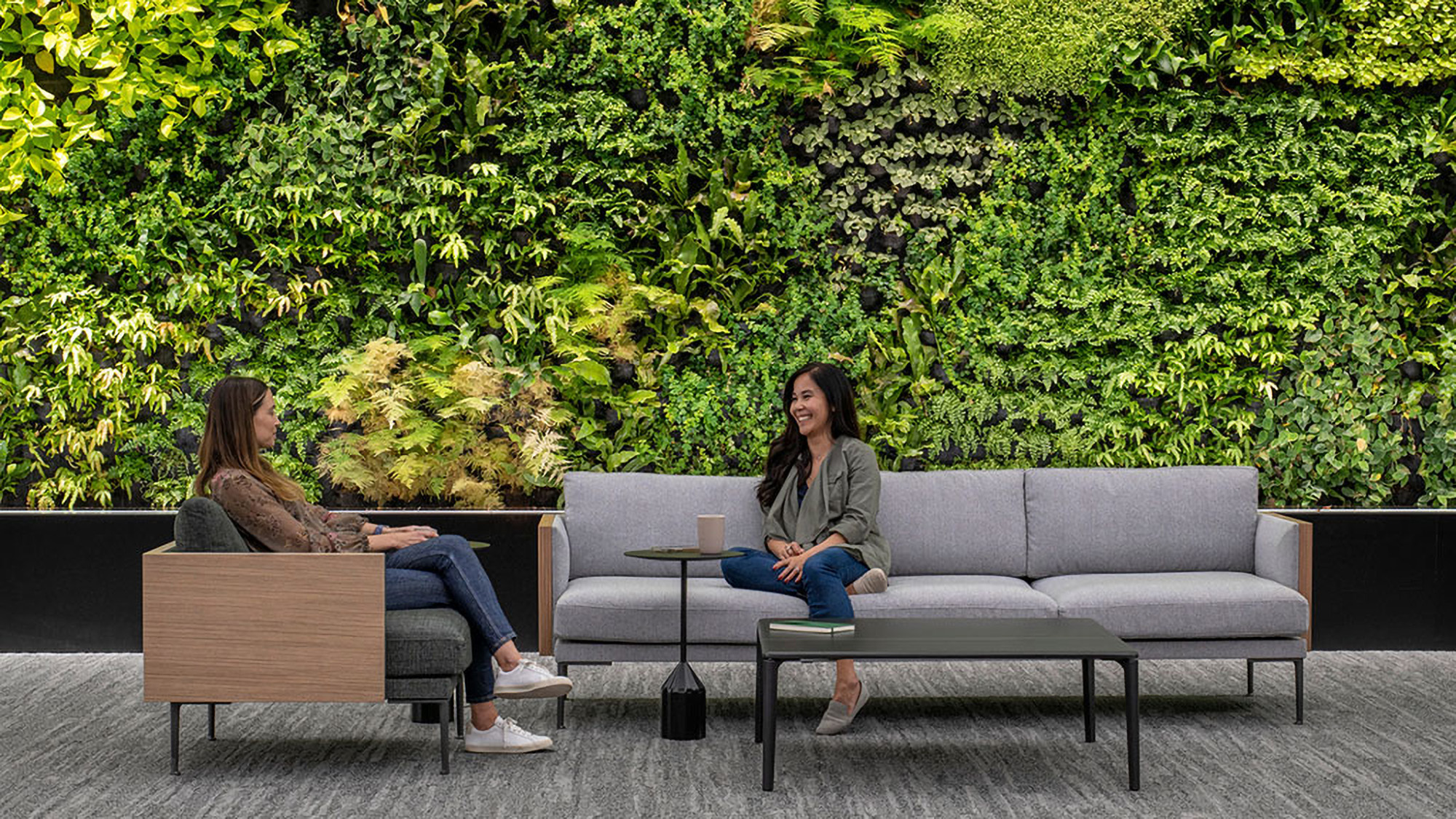 Women sitting on a couch next to a green wall.