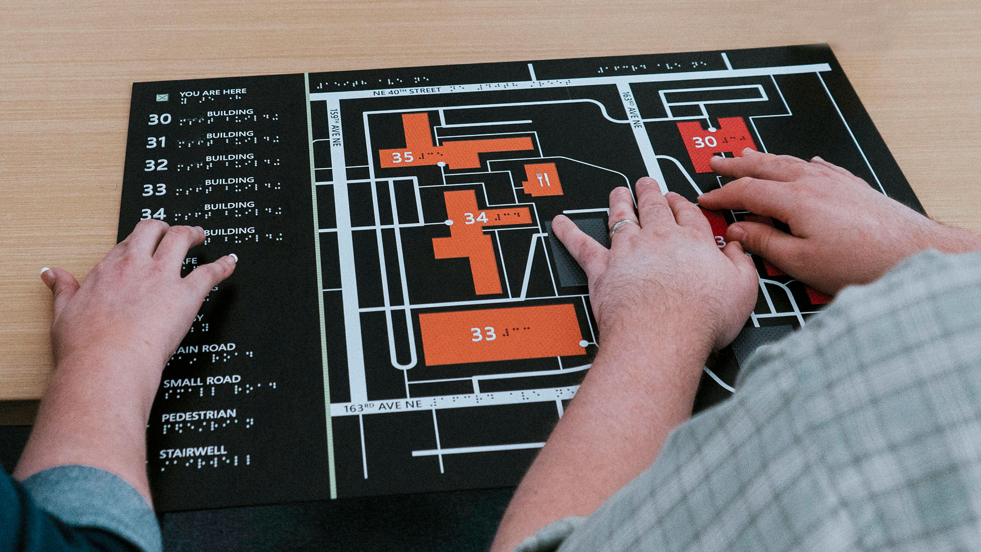 Two people use their hands to navigate a campus using a tactile map.