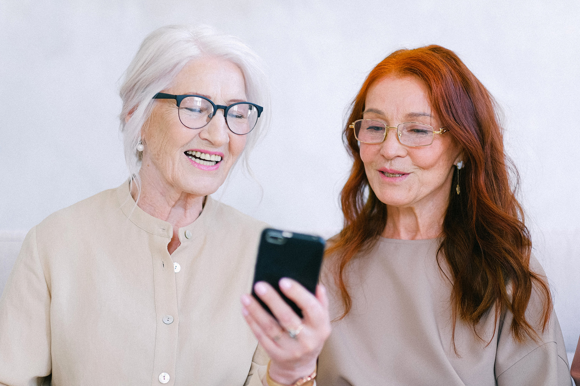 Happy senior women in eyeglasses looking at screen of smartphone