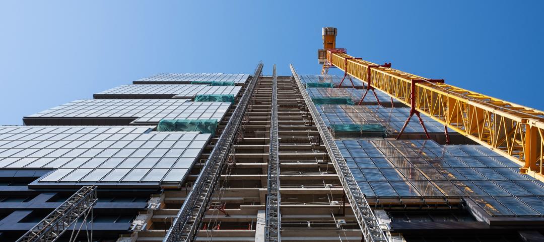 Looking up at the construction site of a skyscraper building with a yellow crane an an exterior elevator