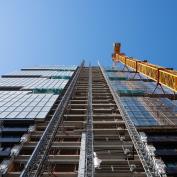 Looking up at the construction site of a skyscraper building with a yellow crane an an exterior elevator